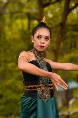 Javanese woman dancing in front of the woods in green costume while in makeup and performing at the village