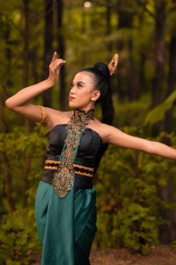 Beautiful Indonesian dancers with traditional green costumes and black tied hair posing inside the forest after performing