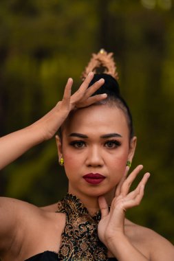Brave Face of an Asian woman in a traditional green costume with golden accessories on her body during the competition in a dance festival in front of the forest