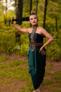 Beautiful Asian woman holding her black hair while standing in front of the forest in a green costume during the festival