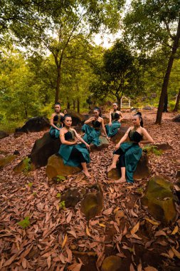 A Group of Asian women takes a vacation to the forest while wearing a green skirt and sitting on a rock during the morning