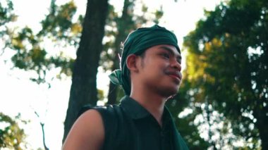 An Asian man with green clothes smiling while meeting her woman in the forest with a tree in the background during the afternoon