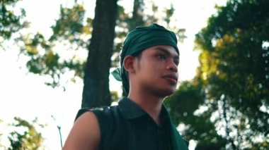 An Asian man with green clothes smiling while meeting her woman in the forest with a tree in the background during the afternoon