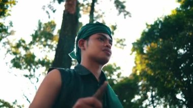 An Asian man with green clothes smiling while meeting her woman in the forest with a tree in the background during the afternoon
