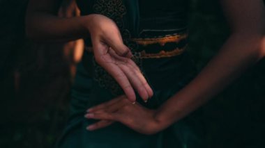 The hand of an Asian woman in a green dress while doing meditation in the forest