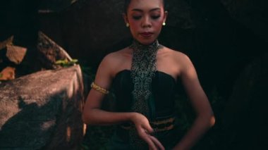 Asian woman in traditional green dress meditating lonely in peacefully in front of the big rock at the mountain during the morning