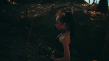 Beautiful Asian woman in green dress walking lonely between the big rocks and trees inside the forest at the mountain