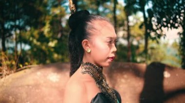 The Face of a Balinese dancer in a black costume while enjoying the mountain view in front of the forest