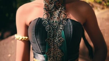 The black hair of an Asian woman with golden jewelry and tied hair in front of the forest during the daylight