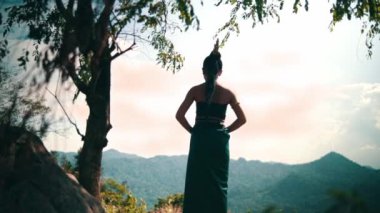 Asian woman with a long dress and black hair standing in front of the canyon to enjoy the view from the top of the mountain during the daylight