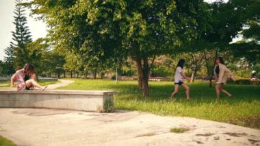 a group of women in shirts dancing with their friends in the middle of a park full of shady trees during the day