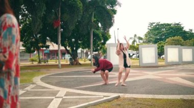 a group of women dancing contemporarily behind a sad woman in a park during the day