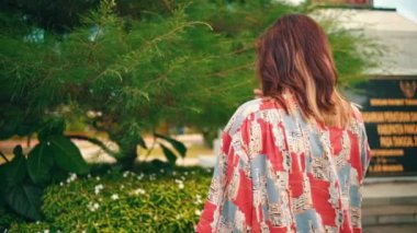 an Asian woman standing in front of a plant full of flowers when she was restless and sad in a garden in the morning