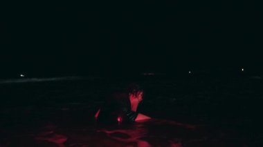 a group of women in black clothes bullied a woman by pushing her into the waves roughly until she cried and fell on a beach at night