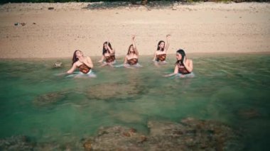 A group of Asian women in white clothes dancing with their friends in the seawater on the beach with white sand on an island during the day