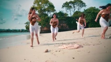 A group of Asian women in white clothes ran and played with their friends on the white sandy beach while on vacation on an island during the day