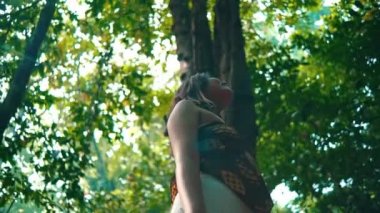 an Asian woman standing in the shade of a tree in the middle of a tropical rainforest on an island alone during the day