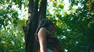 an Asian woman standing in the shade of a tree in the middle of a tropical rainforest on an island alone during the day
