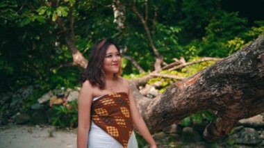 a woman with blonde hair holding a tree trunk while walking on an island for vacation in the morning