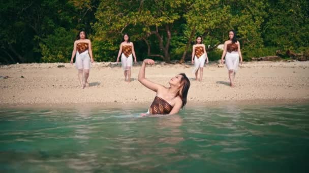 白い服を着たアジア系女性のグループが 日中は島のビーチで青い海の水に浸かっていた友人たちに歩いて行きました — ストック動画