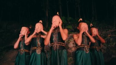 Bir grup Asyalı geleneksel yeşil elbiseli kadın gece kayaların arasında dururken bambu maskeler takıyor.