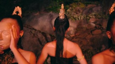 an Asian woman walking among a group of women wearing bamboo masks with smiling faces in front of the rocks at night