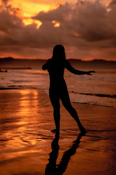 silhouette of an Asian woman dancing ballet with great flexibility and a view of the waves behind her at sunset