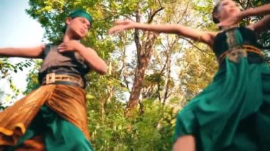 Asyalı bir kadın ve erkek, sabahın erken saatlerinde ormanın ortasında yeşil geleneksel kıyafetler giyerek dans ediyorlar.