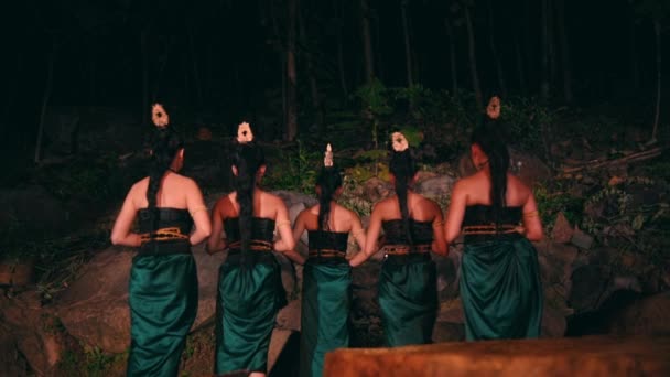 大きな岩の前に立ち竹の仮面を手にしたアジア系の女性たちが夜な夜な森の中で平静な表情で — ストック動画