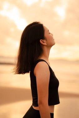 a beautiful Asian woman in black clothes is enjoying the beauty of the beach with a smiling expression on her face while on vacation in the afternoon