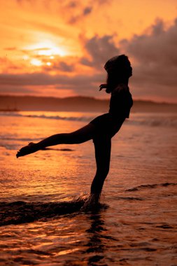 silhouette of an asian woman practicing her ballet moves on the beach with the waves crashing before the festival starts in the afternoon