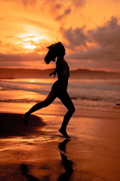 A ballerina with a silhouette shape performs ballet movements very flexibly on the beach with the waves crashing in the afternoon