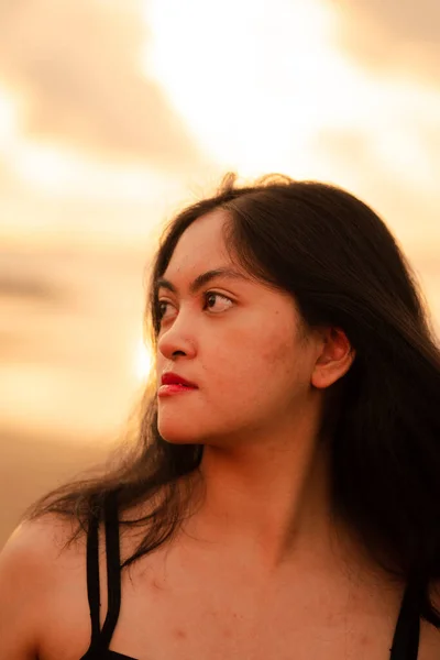 An Asian woman with black hair and a beautiful face posing in front of the beach with warm lighting on the morning