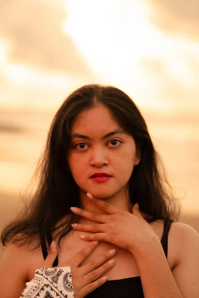 An Asian woman with black hair and a beautiful face posing in front of the beach with warm lighting on the morning