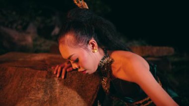 An Asian woman cries when she is about to sit on a rock helplessly and leans against a rock in the middle of a forest at night