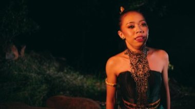 An Asian woman cries when she is about to sit on a rock helplessly and leans against a rock in the middle of a forest at night