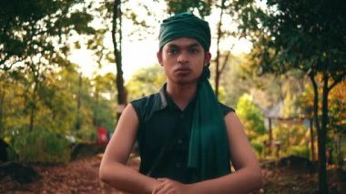 an Asian man in green clothes is standing in the middle of the forest in the morning