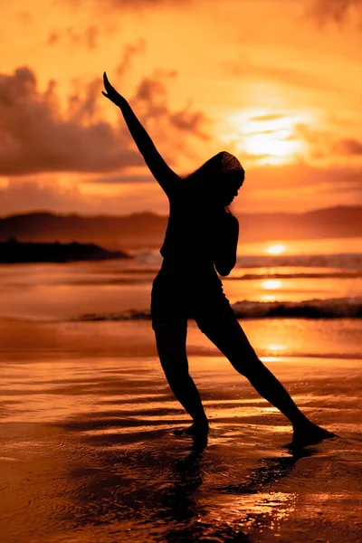 the silhouette of an Asian teenager with a tall body is dancing ballet on the waves on the beach before sunset