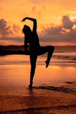 An Asian woman in the form of a silhouette doing ballet movements very agile on the beach in the late afternoon
