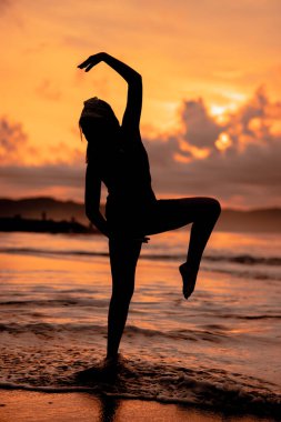 An Asian woman in the form of a silhouette doing ballet movements very agile on the beach in the late afternoon