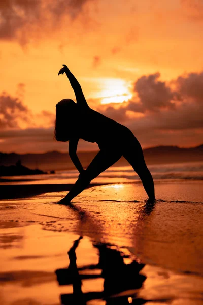 an Asian woman in silhouette is doing gymnastic movements very agile on the beach sand at sunset