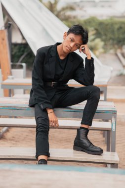 an Asian teenager in a black denim jacket posing by sitting on a cafe chair and relaxing in the afternoon