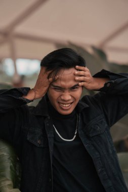 an Asian man in a black denim jacket posing with a cheerful face and very handsome in a cafe during the day
