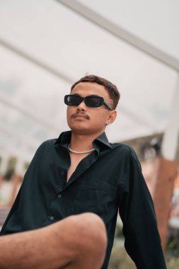 an Asian man with a mustache face wearing a shirt and sunglasses in a very masculine style in the afternoon