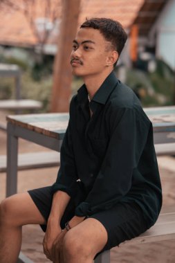 an Asian man with a handsome face and mustache wearing a black shirt while relaxing in the afternoon