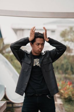 an Asian man is standing beside a cafe table in black leather clothes during the day