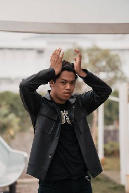 an Asian man is standing beside a cafe table in black leather clothes during the day