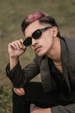 an Asian man with sunglasses and a gray blazer is enjoying the view in the park during the day