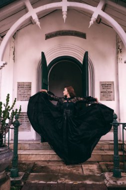 An elegant witch flicks her all black dress in the air in front of the cemetery gates after the Halloween festival begins in the afternoon