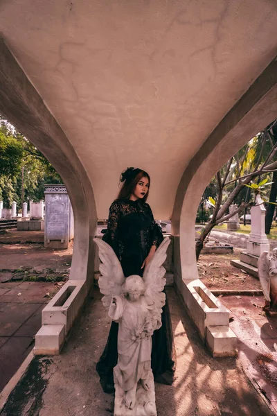 an Asian woman dressed all in black and a scary face was standing over the cemetery in the late afternoon